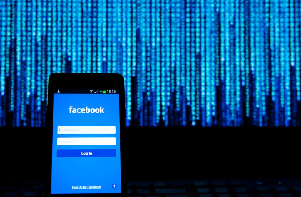 Smartphone with Facebook login screen, set against a blurred backdrop of blue digital data.